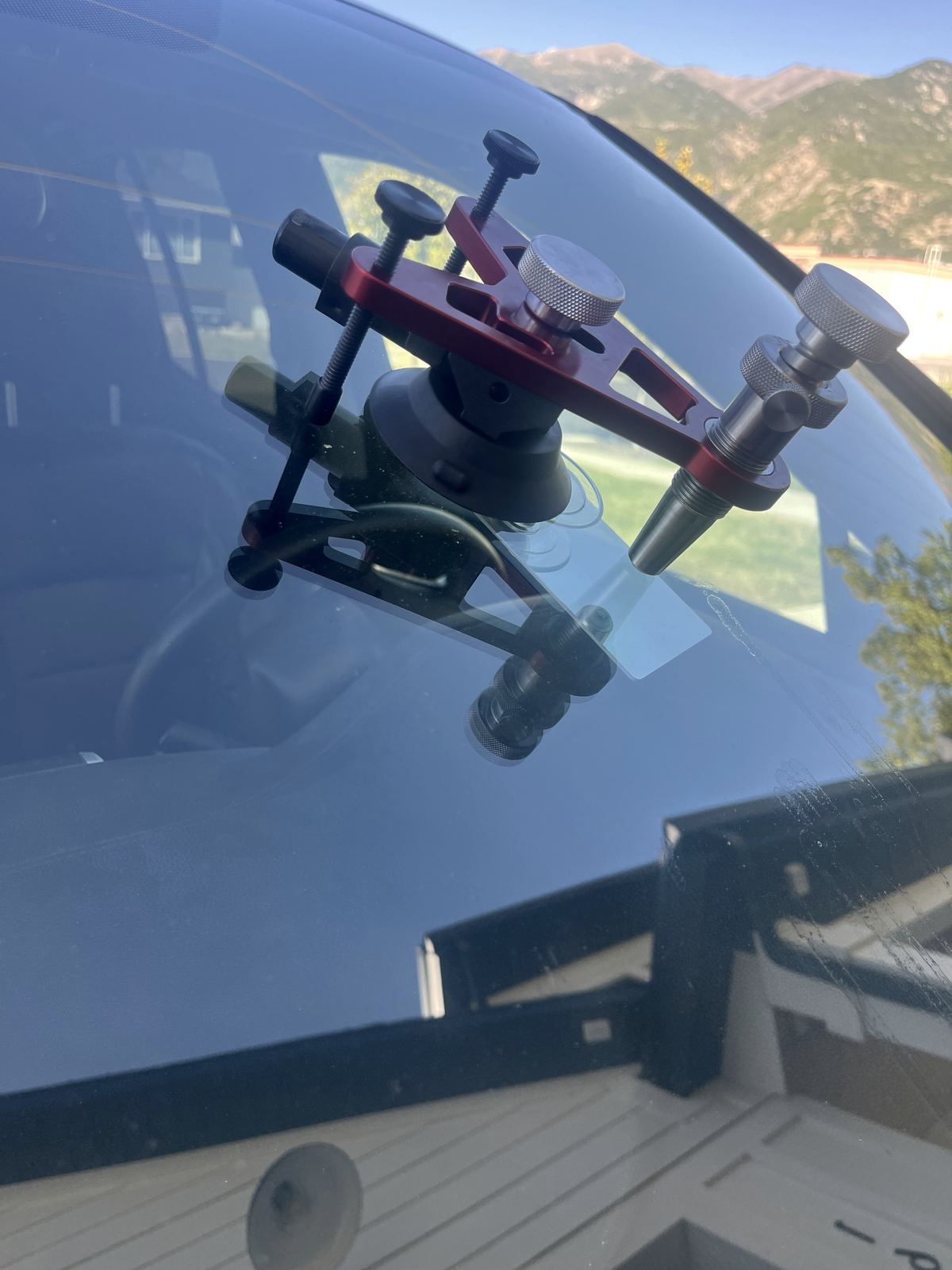 A resin injector clamped over a rock chip on a windshield, with the Wasatch Range behind the glass.